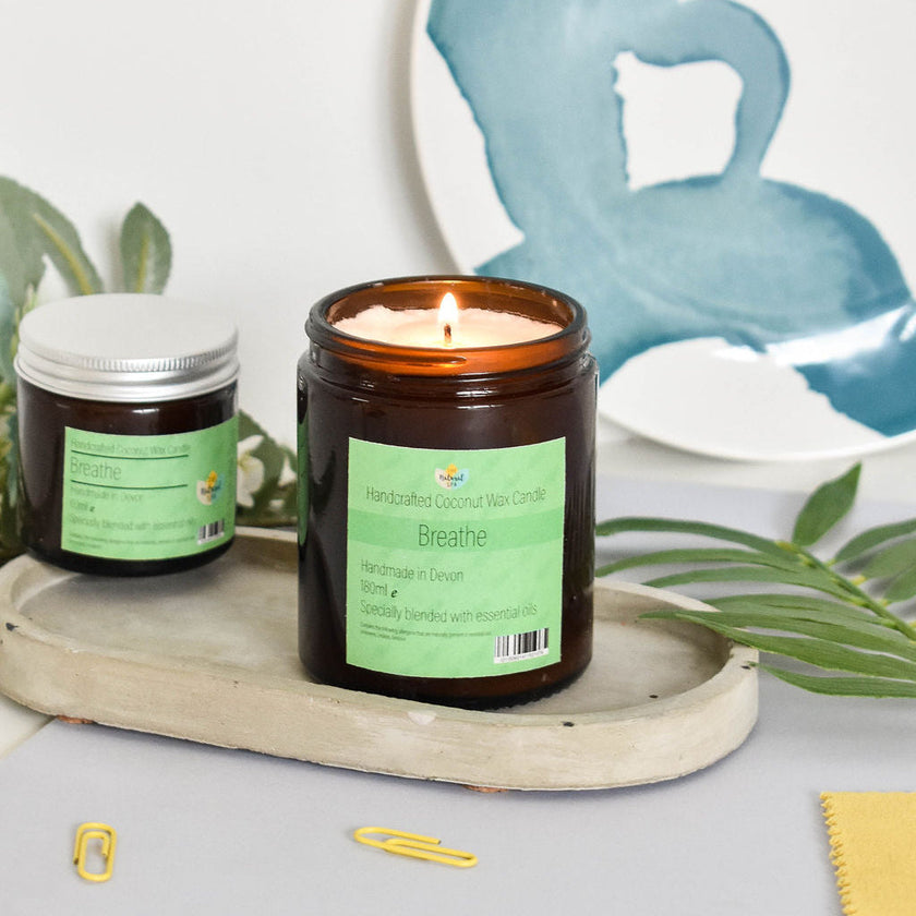 Breathe hand-poured coconut wax candle in amber glass jar with aluminum lid, surrounded by natural elements