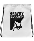 Front of a white Gravity Is a Myth drawstring bag with black cotton straps and one black climber silhouette and lettering design.