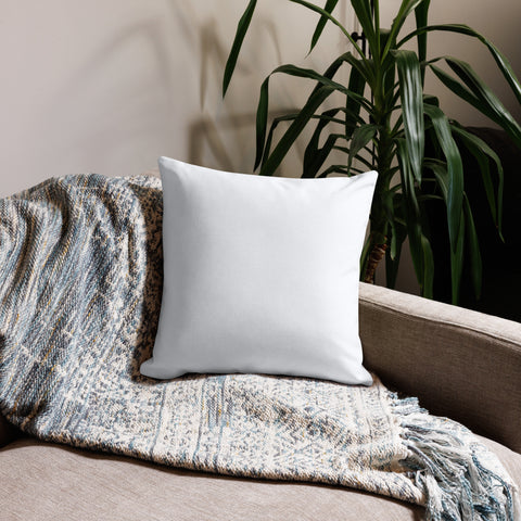White 18 by 18 inch premium throw pillow showing its plain white back, on a sofa with a knitted throw beside a leafy plant.