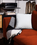 White 18 by 18 inch premium throw pillow showing its plain white back, on a rust-coloured sofa.