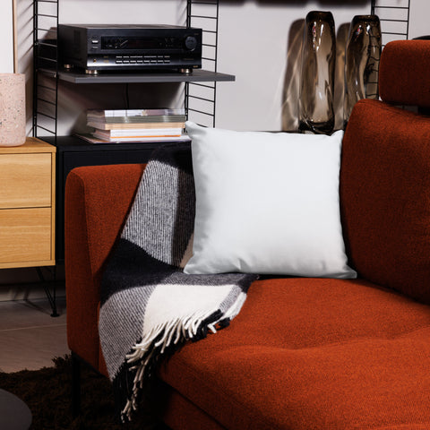 White 18 by 18 inch premium throw pillow showing its plain white back, on a rust-coloured sofa.