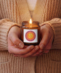 Vibrant Om Mandala Christmas Warmth 4 oz soy candle in an amber glass jar, held by a person wearing a beige knitted cardigan, with one complete colourful mandala front label.
