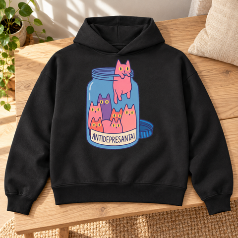 Black heavyweight hoodie with colourful Antidepresantai cat jar front print, laid on an oak bench beside a linen cushion and houseplant.