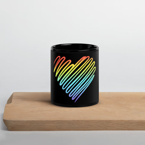 Rainbow Heart 11 oz black glossy ceramic mug on a light wooden serving tray against a pale grey wall, showing its single colourful heart front print.