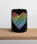 Rainbow Heart 15 oz black glossy ceramic mug on a light wooden serving tray against a pale grey wall, showing its single colourful heart front print.