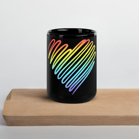 Rainbow Heart 15 oz black glossy ceramic mug on a light wooden serving tray against a pale grey wall, showing its single colourful heart front print.