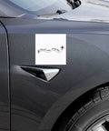 Travel More, Worry Less 5 × 5 inch white car magnet displayed on the front side panel of a dark grey car, with one complete black travel quote and aeroplane design.