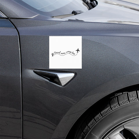 Travel More, Worry Less 5 × 5 inch white car magnet displayed on the front side panel of a dark grey car, with one complete black travel quote and aeroplane design.