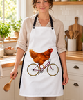 Chicken on a Bicycle white apron worn by a cook in a sunlit kitchen, with the complete brown hen and purple bicycle design visible