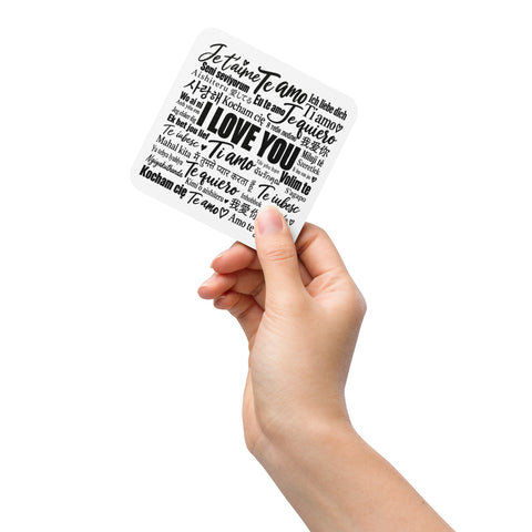 A hand holding the Love in Every Language cork-back coaster.