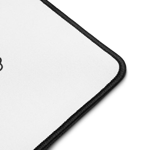 Close-up of the white polyester surface and black hemmed corner of the Overthink This desk mat.