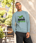 Model wearing the Agave Dinosaur Motivation men’s heavyweight long-sleeve tee on a sunlit cafe terrace beside a pale stone wall and greenery, showing its single front print.