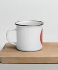 White 12 oz enamel mug with a silver rim and a pink, purple and golden-orange Om mandala on the front, shown on a wooden board; left-side view.