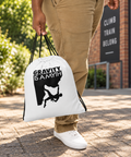 White Gravity Is a Myth drawstring bag carried along a sunlit path outside a climbing gym, with its single black front design visible.
