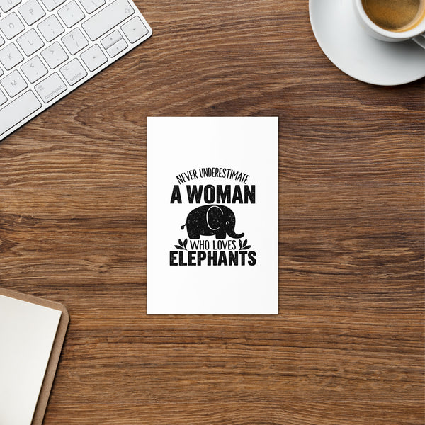 Elephant Lover 4 × 6 inch greeting card on a wooden desk beside coffee, a keyboard and a notebook, showing one black elephant design on the front.