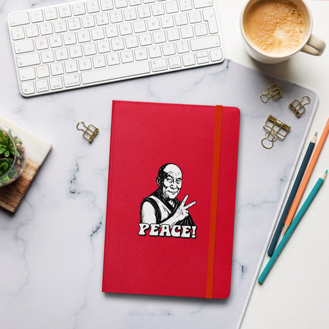 Red Peace Sign Monk hardcover lined notebook on a desk beside coffee, a white keyboard and pencils, showing one complete black-and-white monk and PEACE! front design.