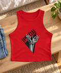 Red Įpročiai graphic racer tank laid flat on a wooden bench beside blue jeans and a green plant in natural daylight.