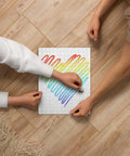 Rainbow Heart 252-piece jigsaw puzzle with one complete colourful heart on a white background, being assembled by two people on a wooden table.