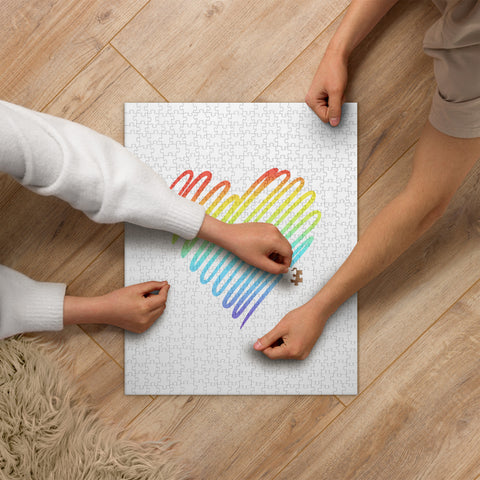 Rainbow Heart 520-piece jigsaw puzzle with one complete colourful heart and surrounding white space, being assembled by two people on a wooden table.