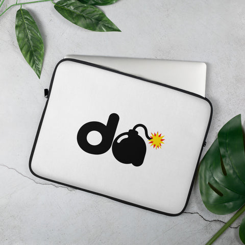 15-inch white D-Bomb Spark laptop sleeve with black trim and black D and cartoon bomb artwork with a yellow-red spark, shown with a laptop and green leaves.