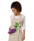 Woman wearing a Rope organic cotton apron with green leafy Earth artwork and Go Green lettering above a two-compartment pocket.