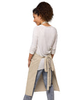 Woman wearing a Rope organic cotton apron with green leafy Earth artwork and Go Green lettering above a two-compartment pocket.