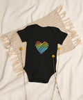 The black Rainbow Heart organic cotton baby bodysuit laid on cream bedding.