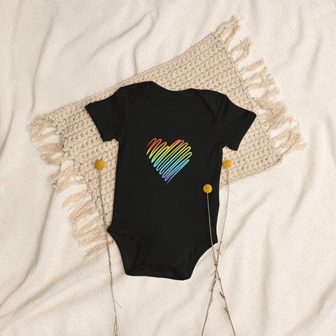 The black Rainbow Heart organic cotton baby bodysuit laid on cream bedding.