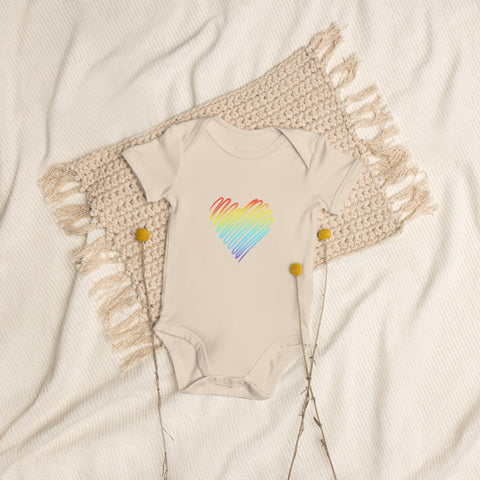 The organic natural Rainbow Heart organic cotton baby bodysuit laid on cream bedding.
