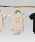 The organic natural Rainbow Heart organic cotton baby bodysuit hanging on a clothes rail.