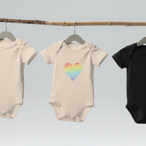The organic natural Rainbow Heart organic cotton baby bodysuit hanging on a clothes rail.