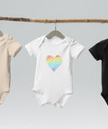 The white Rainbow Heart organic cotton baby bodysuit hanging on a clothes rail.