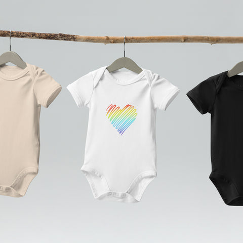 The white Rainbow Heart organic cotton baby bodysuit hanging on a clothes rail.