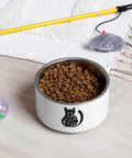One Cat Away from Crazy 18 oz white stainless steel pet bowl filled with dry food on a pale wooden floor beside colourful cat toys, showing one complete black cat-shaped front print.