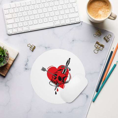 Pierced Skull Heart round mouse pad on a pale marble desk beside a keyboard, coffee and coloured pencils, showing one tattoo-style design and a curled edge.
