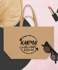 Latte recycled cotton shopping bag with a black Karma brushstroke quote, styled with a fan, sunglasses, and lipstick on a pink background.