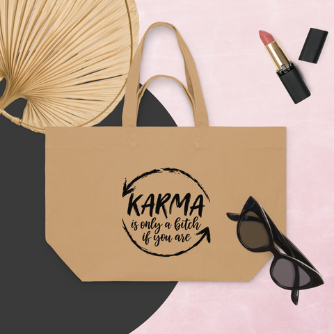 Latte recycled cotton shopping bag with a black Karma brushstroke quote, styled with a fan, sunglasses, and lipstick on a pink background.