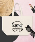 Natural Raw recycled cotton shopping bag with a black Karma brushstroke quote, styled with a fan, sunglasses, and lipstick on a pink background.