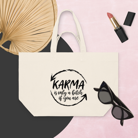 Natural Raw recycled cotton shopping bag with a black Karma brushstroke quote, styled with a fan, sunglasses, and lipstick on a pink background.