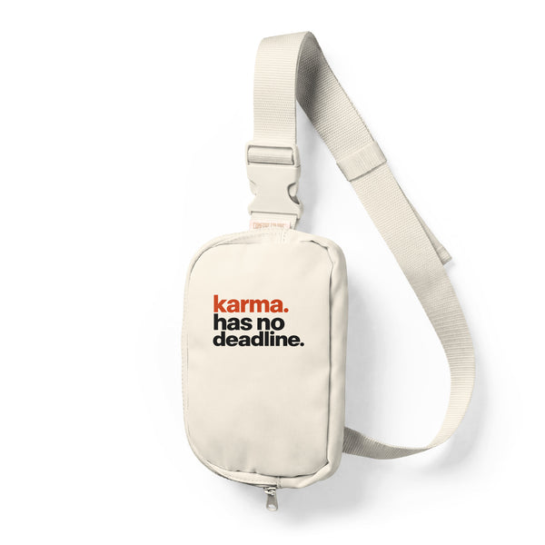 Ivory sling bag with full orange and black Karma Has No Deadline lettering high on the front