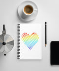 Rainbow Heart dotted spiral notebook on a white desk beside coffee, a moka pot, a pen and a phone.