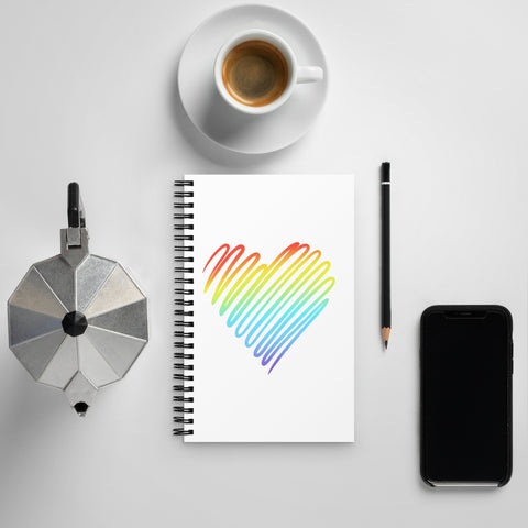 Rainbow Heart dotted spiral notebook on a white desk beside coffee, a moka pot, a pen and a phone.