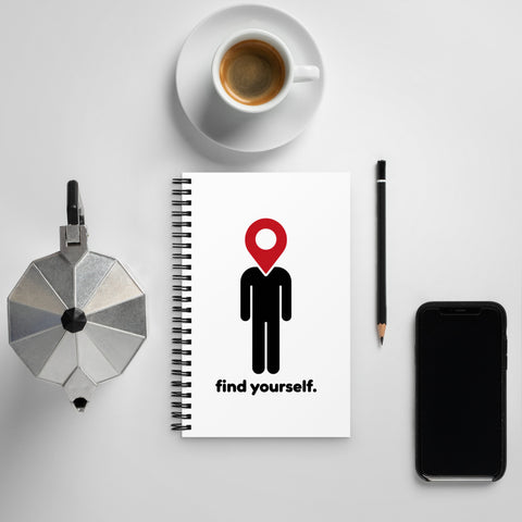 Find Yourself spiral notebook with a red location-pin figure on a desk beside coffee, a pencil, a moka pot, and a phone.