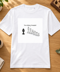 White Tavo ėjimas, brangioji heavyweight T-shirt with cheeky chess artwork, laid on an oak table beside coffee and a chessboard.