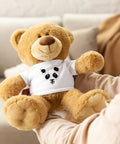 Golden-brown Ink Splatter Panda teddy bear seated on a beige sofa, wearing a white T-shirt with one complete black panda face print on the front.