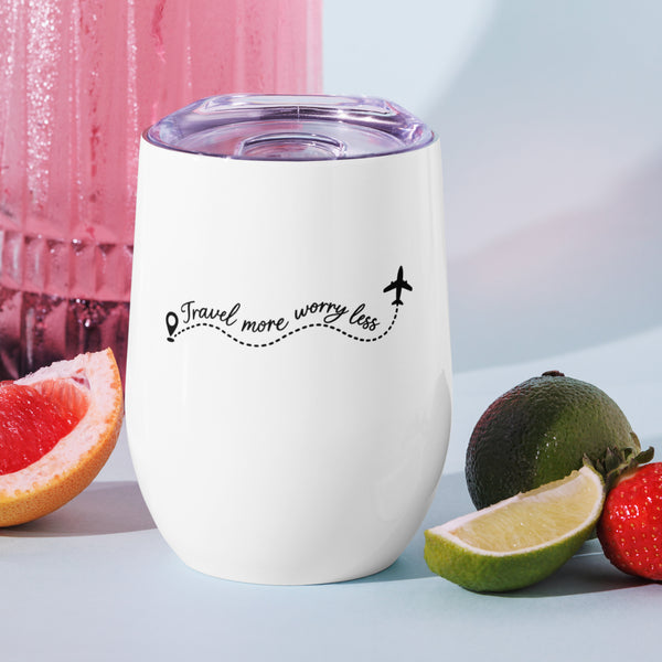 White Travel More, Worry Less insulated wine tumbler with a lid and one black front design, standing beside grapefruit and limes.