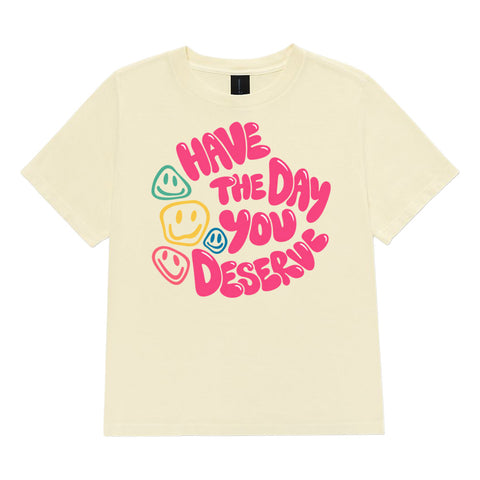 Buttermilk women's heavyweight garment-dyed tee, front view with pink Have the Day You Deserve lettering and colourful smiley faces.