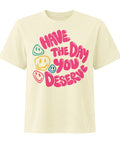 Buttermilk women's heavyweight garment-dyed tee, front view with pink Have the Day You Deserve lettering and colourful smiley faces.