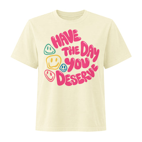 Buttermilk women's heavyweight garment-dyed tee, front view with pink Have the Day You Deserve lettering and colourful smiley faces.